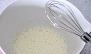 Dubenyje išplakite kiaušinius, suberkite cukraus pudrą ir plakite, kol susidarys purus, burbuliuojantis mišinys.