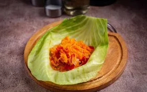 Dabar padėkite vieną kopūsto lapą ant lygaus paviršiaus ir į vidurį įdėkite 2–3 šaukštus daržovių įdaro. Susukite kopūsto lapą į voką, ka...