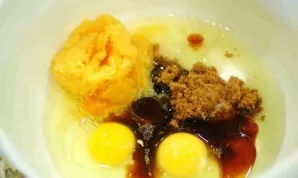 Kitame dubenyje įpilkite 0,5 puodelio rudojo cukraus, augalinio aliejaus, kiaušinių, tarkuoto žalio moliūgų ir vanilės.