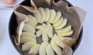 Nulupkite obuolius ir supjaustykite juos plonais griežinėliais, kepimo indą išklokite kepimo popieriumi ir išdėliokite obuolius.