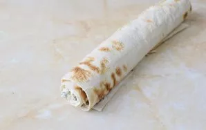 Lavašą su įdaru susukite į vyniotinį. Apvyniokite jį maistine plėvele ir 2–3 valandas padėkite į šaldytuvą, kad įsigertų.