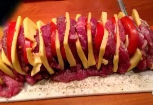 Į kiekvieną mėsos gabalėlį įdėkite pomidoro griežinėlį, sūrio griežinėlį ir porą česnako gabalėlių.