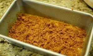 Kepimo indą ištepkite sviestu, supilkite pusę tešlos, tada suberkite pusę sausų trupinių iš trintuvo.