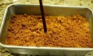 Supilkite likusią tešlą ir suberkite likusius trupinius, pagaliuku šiek tiek pamaišykite tešlą.