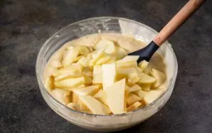 Į dubenį su tešla sudėkite obuolių griežinėlius.